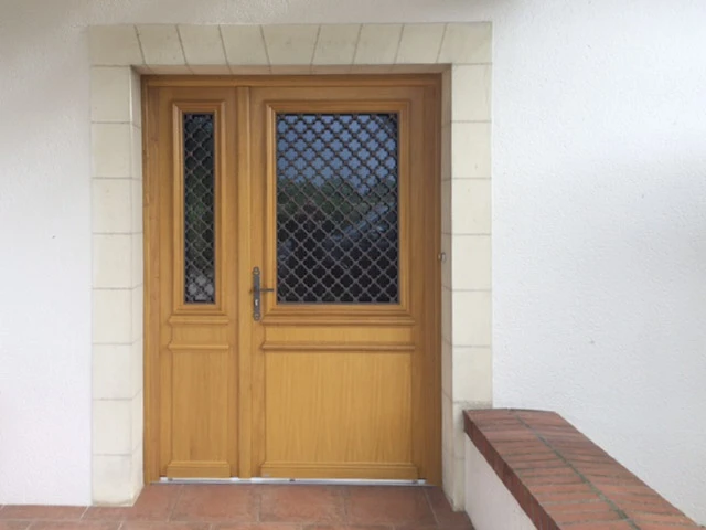 Entrée extérieure d'une maison avec porte en bois massif à deux vantaux, vitrage sécurisé par grillage métallique losangé