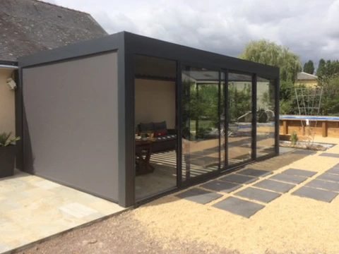 Extension contemporaine à structure métallique noire et baies vitrées coulissantes, située dans un jardin résidentiel avec terrasse dallée