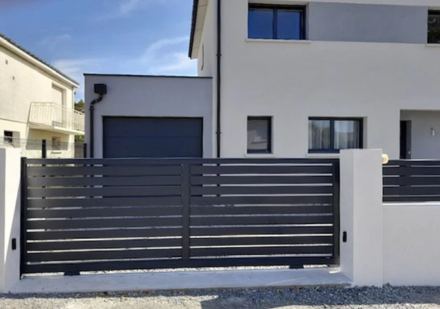 Extérieur résidentiel montrant une porte de garage sectionnelle moderne gris anthracite avec quatre hublots circulaires alignés dans le panneau supérieur