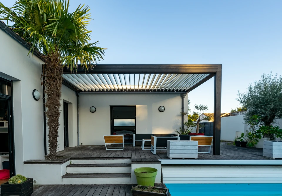 Patio extérieur moderne avec des sièges confortables, pergola, et pelouse bien entretenue dans la lumière du soir